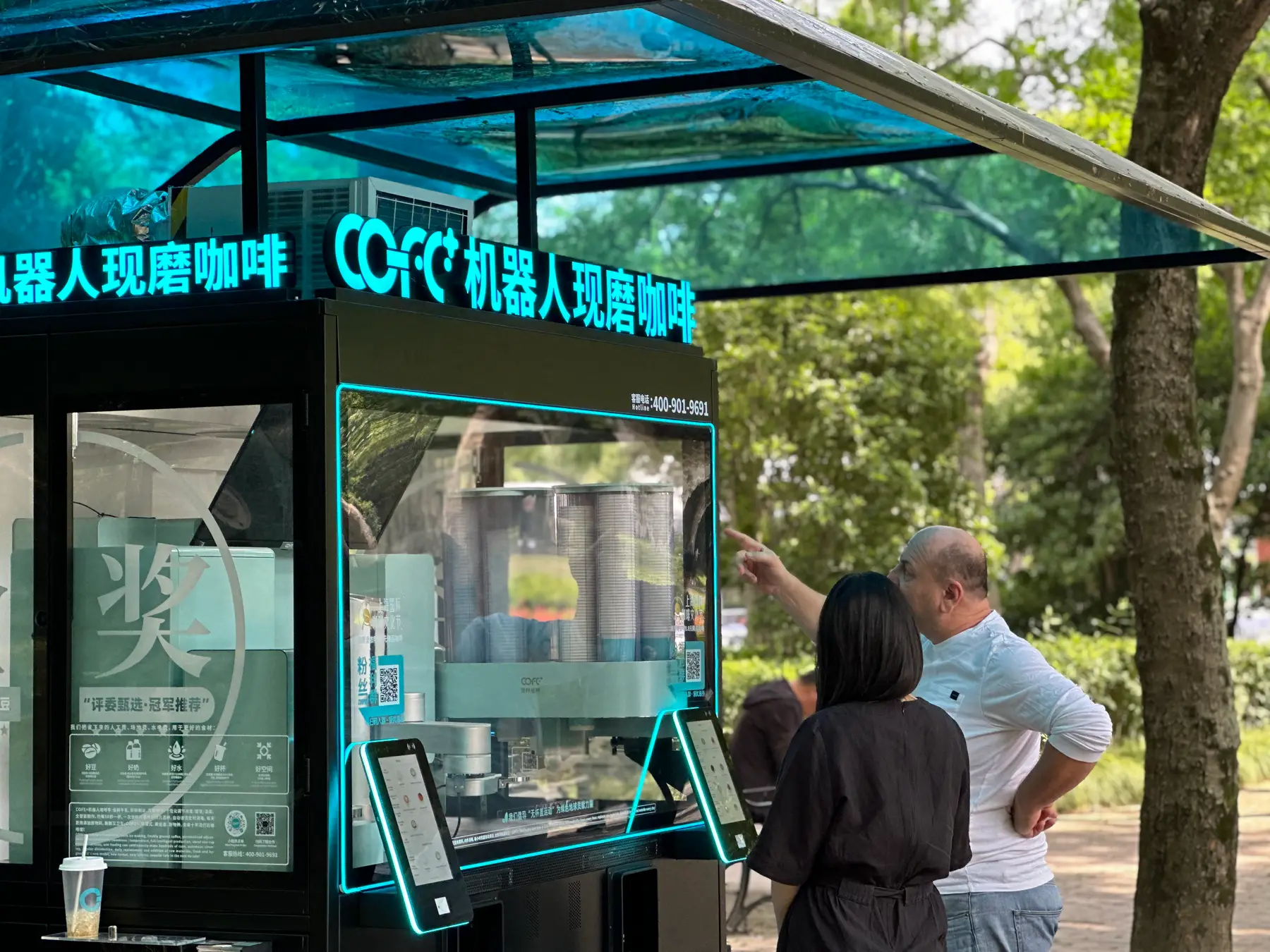 Autonomous coffee kiosk in an outdoor park setting with users nearby.